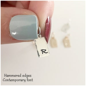 May include: A silver charm with a hammered finish and a contemporary font 'R' on a rectangular tag.