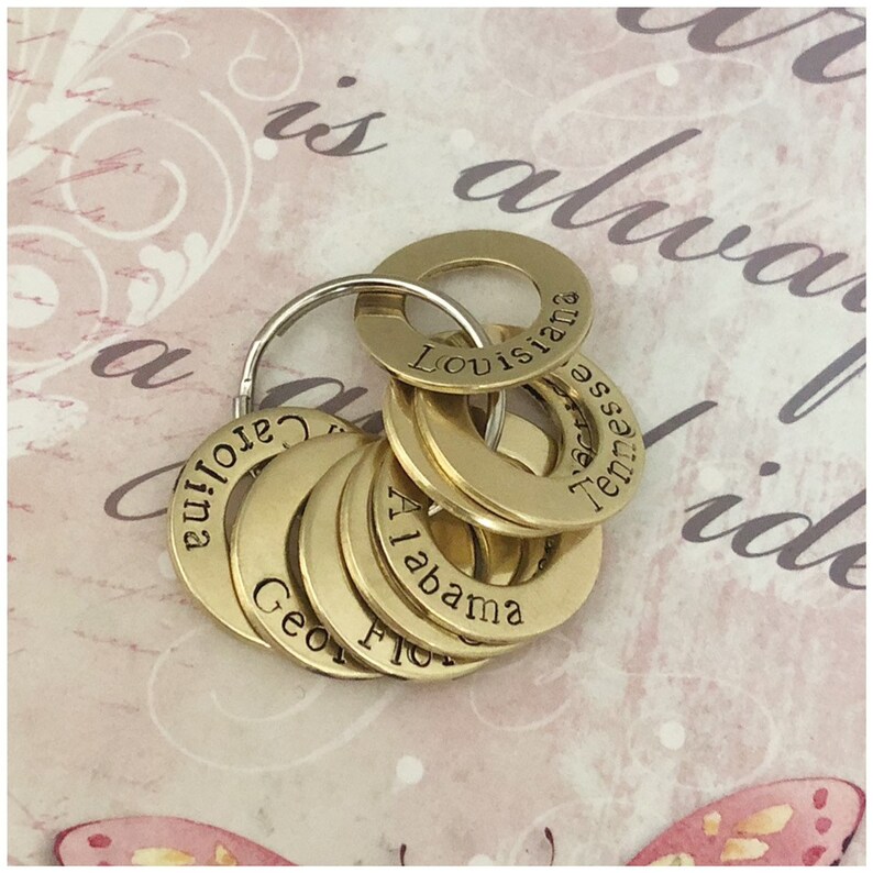 Puede incluir: Un juego de llaveros de lat&oacute;n con los nombres de diferentes estados grabados en ellos, incluyendo "Louisiana", "Tennessee", "Alabama", "Georgia" y "Florida".