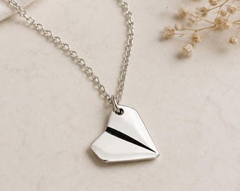 May include: A silver-toned necklace featuring a pendant shaped like a folded paper airplane. The pendant has a smooth, reflective surface with a single dark line running through the center, suspended from a delicate silver-toned metal chain link.
