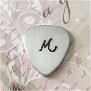 May include: A silver guitar pick with the letter "M" engraved on it.