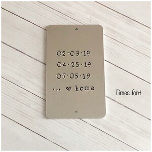 Puede incluir: Una placa rectangular de metal plateado con esquinas redondeadas y dos peque&ntilde;os agujeros en la parte superior e inferior. La placa est&aacute; estampada con las fechas 02.03.19, 04.25.19, 07.05.19 y el texto ... &hearts; home. A la derecha dice Times font.