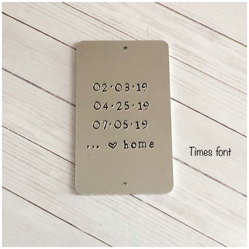 Puede incluir: Una placa rectangular de metal plateado con esquinas redondeadas y dos peque&ntilde;os agujeros en la parte superior e inferior. La placa est&aacute; estampada con las fechas 02.03.19, 04.25.19, 07.05.19 y el texto ... &hearts; home. A la derecha dice Times font.