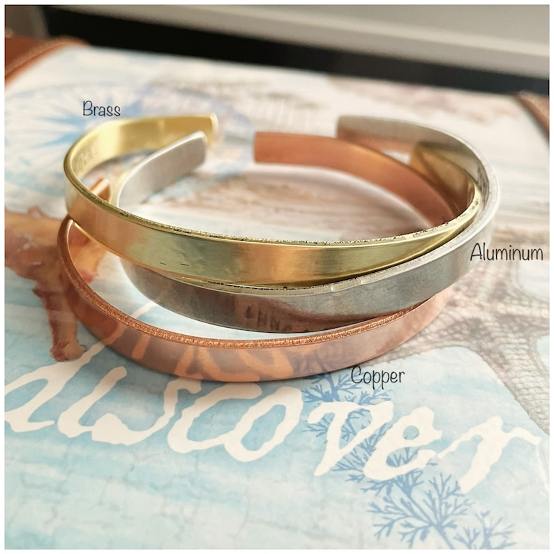 Puede incluir: Tres pulseras de metal apiladas en lat&oacute;n, aluminio y cobre. Las pulseras son todas lisas y tienen un acabado suave.