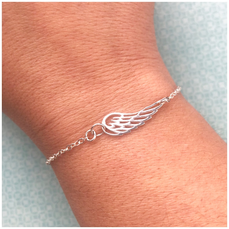 Puede incluir: Un brazalete de cadena de plata con un delicado dije de ala de &aacute;ngel.