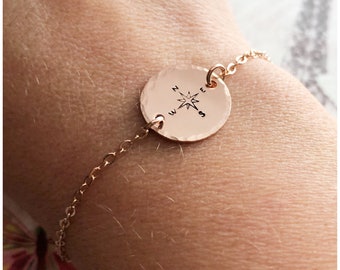 May include: A rose gold bracelet with a compass charm. The charm is round and has a hammered texture. The compass points are engraved with the letters N, S, E, and W.