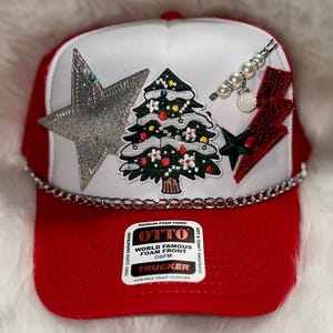 May include: Red and white trucker hat with a silver star, a Christmas tree, and a red lightning bolt patch. The hat has a chain detail and a label that reads "OTTO World Famous Foam Front OSFM Trucker Durable Snap Closure".