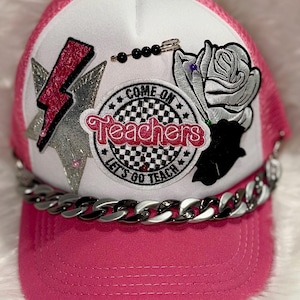 May include: Pink and white trucker hat with a silver star, a pink lightning bolt, a black and white checkered patch that says "Come on Teachers Let's Go Teach", a silver rose, and a silver chain.