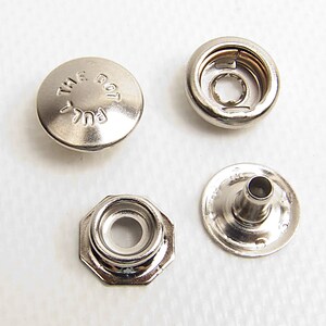 May include: A set of four silver-colored metal snap fastener components. One circular cap is embossed with the text PULL THE DOT. The set includes a socket, a stud with a central post, and a circular base piece, all featuring a metallic finish.