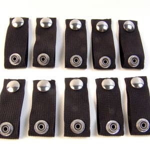 May include: Ten black fabric straps with silver metal snaps. Each strap has two snaps.