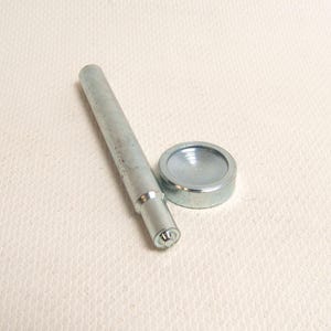 May include: A set of metal tools, including a cylindrical punch and a circular die. The punch is silver and has a flat end. The die is a small, circular piece with a concave center. The tools are likely used for setting rivets or other fasteners.