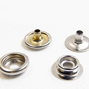 Puede incluir: Cuatro botones a presión de metal, dos plateados y dos dorados. Los botones a presión se utilizan para unir tela o cuero.