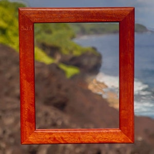 May include: A red wooden picture frame with a view of a rocky coastline and ocean through the frame.
