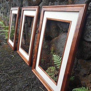Peut inclure: Trois cadres photo en bois avec un passe-partout blanc et une finition en bois naturel. Les cadres sont disposés en rangée, le plus grand à droite et le plus petit à gauche.