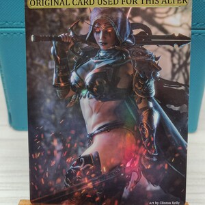 May include: A fantasy illustration of a female elf warrior with glowing red eyes, wearing armor and holding a sword. The background is a dark forest with glowing embers. The text "ORIGINAL CARD USED FOR THIS ALTER" is at the top of the image. The text "Art by Clinton Kelly" is at the bottom of the image.