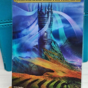May include: A fantasy art print featuring a tall, gray stone tower with a pointed roof, set against a backdrop of a blue sky with swirling clouds and a distant mountain range. The tower is perched on a rocky outcrop, with a grassy hillside in the foreground. The print has a vibrant color palette, with shades of blue, green, purple, and orange.