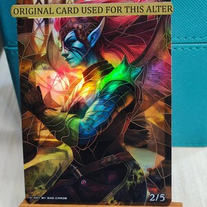 Può includere: Una carta d'arte fantasy con un'elfo dalla pelle blu e capelli rossi, vestita di un'armatura e che tiene un globo luminoso. La carta ha un effetto a vetri colorati e il testo "ORIGINAL CARD USED FOR THIS ALTER" e "2/5".