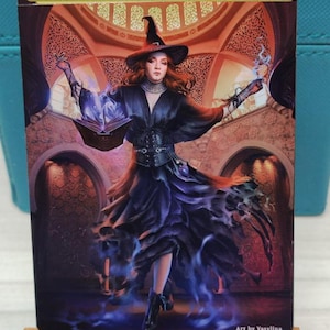 May include: A woman in a black dress and witch's hat stands in a room with arched doorways. She is holding a book and a glowing orb. The text "ORIGINAL CARD USED FOR THIS ALTER" is at the top of the image. The text "Art by Vasyllina" is at the bottom of the image.
