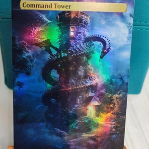 May include: A fantasy-themed trading card with a holographic finish. The card features a stone tower with a dragon wrapped around it. The card's title is "Command Tower".
