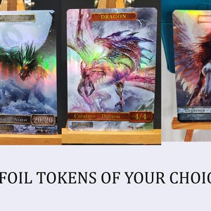 Peut inclure: Trois cartes de jeu à collectionner en feuille avec des motifs holographiques. Les cartes représentent un dragon vert, un dragon rouge et un ange blanc. Les cartes sont exposées sur de petits chevalets en bois. Le texte sur les cartes indique "DRAGON", "ANGEL" et "Avatar 20/20".