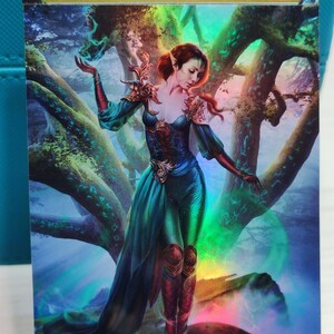 Peut inclure: Une carte d'art fantastique représentant une femme aux cheveux roux et aux yeux verts debout dans une forêt. La femme porte une robe verte et bleue avec des accents dorés. L'arrière-plan est une forêt avec des arbres et un ciel bleu. La carte porte le texte "ORIGINAL CARD USED FOR THIS ALTER" en haut.