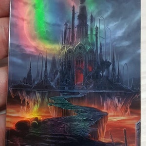 May include: A fantasy art print of a dark, gothic castle on a cliff overlooking a fiery landscape. The castle has tall spires and a large, arched entrance. The sky is a dark blue with a rainbow-colored moon. The text "ORIGINAL CARD USED FOR THIS ALTER" is at the top of the print. The text "Art by Olga Fomina" is at the bottom of the print.