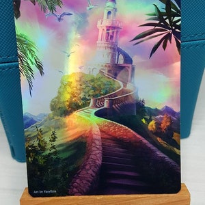 May include: A fantasy-themed altered card featuring a white tower on a hill with a winding staircase leading up to it. The background is a colorful gradient with clouds and birds flying in the sky. The text "ORIGINAL CARD USED FOR THIS ALTER" is at the top of the card. The text "Art by Vasyllina" is at the bottom of the card.