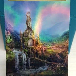 May include: A fantasy art print of a tall, spiraling tower with a waterfall cascading down the side. The tower is surrounded by lush green hills and a rainbow appears in the sky. The text "ORIGINAL CARD USED FOR THIS ALTER" is at the top of the print. The text "Art by Nadegda Mihalova" is at the bottom of the print.