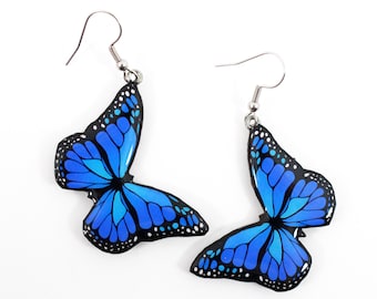 May include: A pair of blue butterfly earrings with silver hooks. The butterflies have black outlines and white spots.
