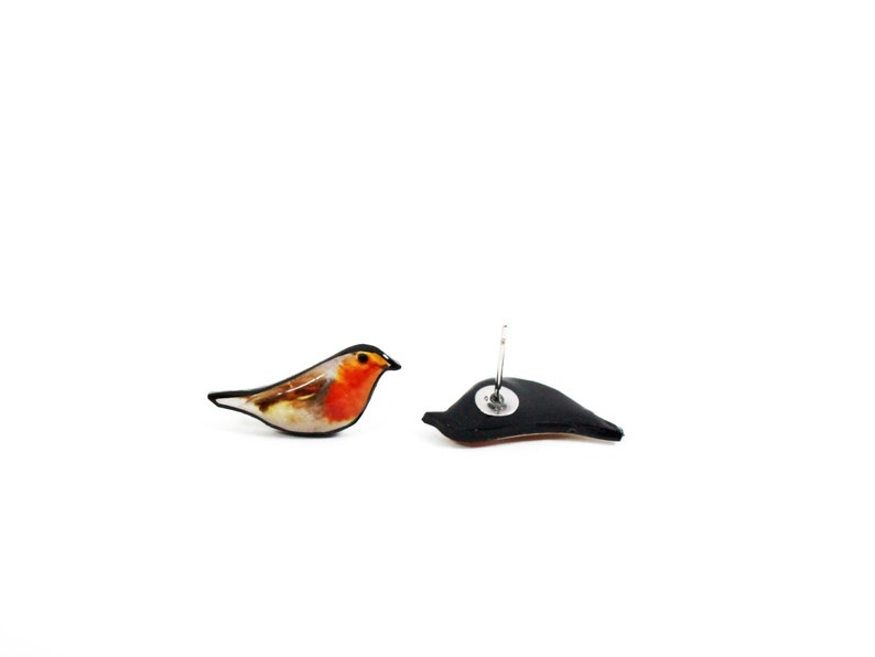 May include: A pair of earrings featuring a robin bird design. The earrings are made of polymer clay and have a black background with a detailed image of a robin bird. The earrings are attached to silver posts.