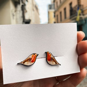 May include: A pair of robin bird earrings. The earrings are made of wood and painted with realistic details. The robins are facing to the right.