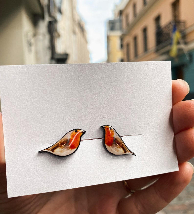 May include: A pair of robin bird earrings. The earrings are made of wood and painted with realistic details. The robins are facing to the right.