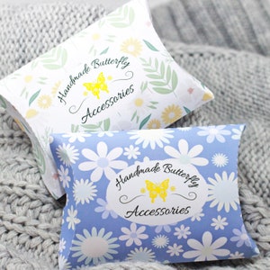 May include: Two pillow boxes with a floral pattern and the text "Handmade Butterfly Accessories" on the front. The top box is white with green leaves and yellow flowers. The bottom box is blue with white flowers.