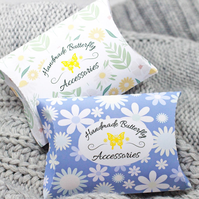 May include: Two pillow boxes with a floral pattern and the text "Handmade Butterfly Accessories" on the front. The top box is white with green leaves and yellow flowers. The bottom box is blue with white flowers.