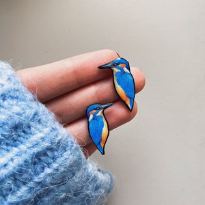 May include: A pair of blue and orange bird earrings. The birds are facing opposite directions and have black eyes and beaks.
