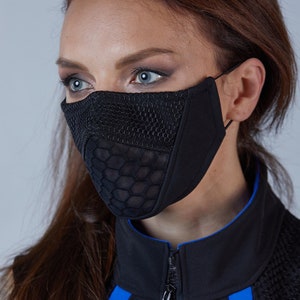 Puede incluir: Una mujer con una chaqueta negra sin mangas con detalles azules y una máscara facial negra con un patrón geométrico.