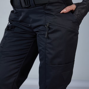 Puede incluir: Pantal&oacute;n cargo negro con m&uacute;ltiples bolsillos y cintur&oacute;n. El pantal&oacute;n tiene un bolsillo con cremallera en la pierna derecha y un parche triangular en la pierna izquierda.