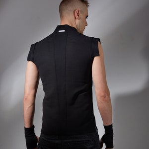 May include: A black sleeveless shirt with a high collar and a small silver label on the back. The shirt is worn over black jeans.
