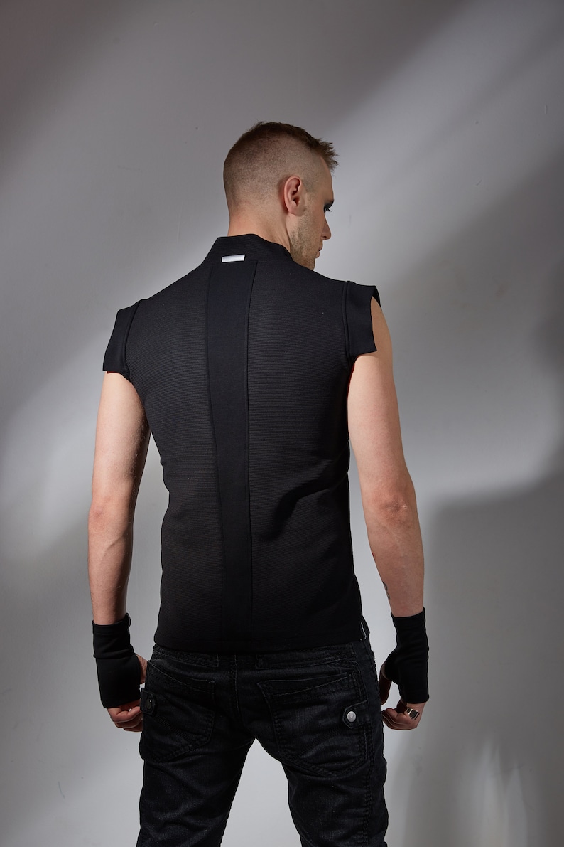 May include: A black sleeveless shirt with a high collar and a small silver label on the back. The shirt is worn over black jeans.