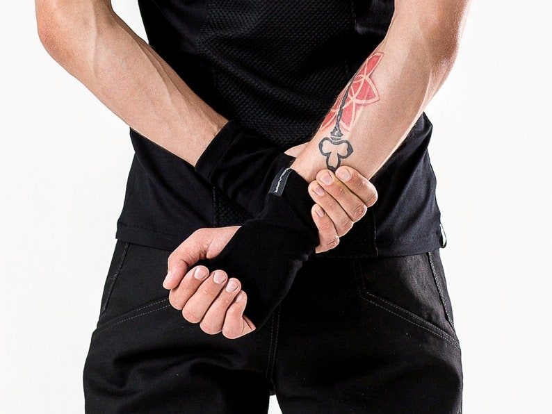 May include: A person wearing a black shirt and black pants with a black wrist warmer on their left wrist. The person has a tattoo on their left forearm.