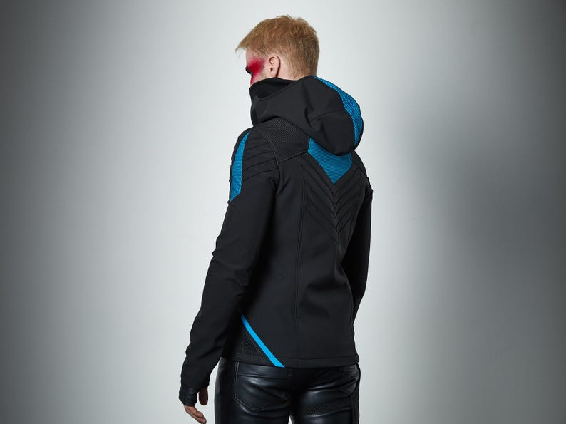 May include: A black hooded jacket featuring teal blue accents on the shoulders and back. The jacket includes a high collar, long sleeves, and a chevron-patterned quilted design on the back panel. The garment is paired with black trousers.