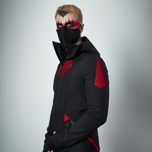 May include: A black hooded jacket featuring a high collar, a full-length front zipper, and red textured panels on the chest, shoulders, and lower sides. The jacket is worn with a black textured face mask covering the nose and mouth area.