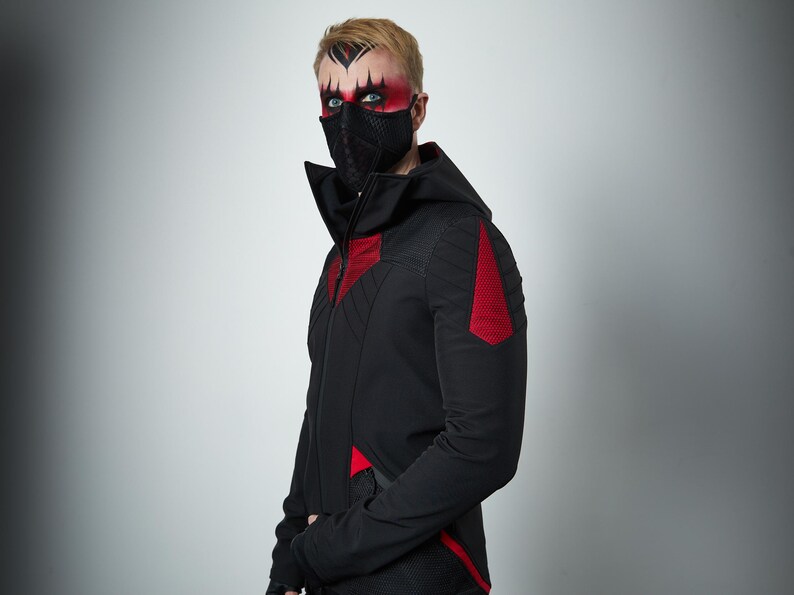 May include: A black hooded jacket featuring a high collar, a full-length front zipper, and red textured panels on the chest, shoulders, and lower sides. The jacket is worn with a black textured face mask covering the nose and mouth area.