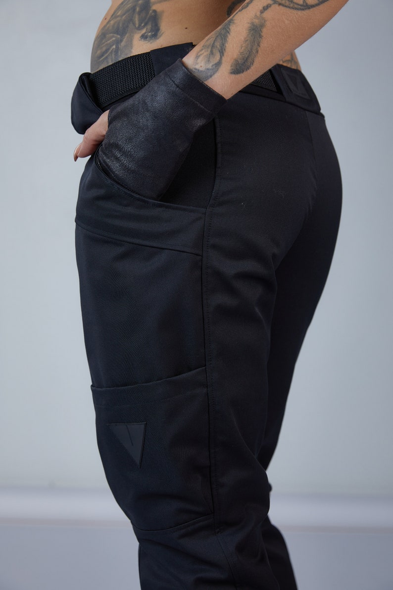 Puede incluir: Pantal&oacute;n negro con un gran bolsillo cargo en la pierna izquierda. El bolsillo tiene un parche triangular con un logotipo.
