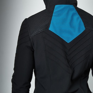 May include: A black hooded jacket featuring a vibrant blue hexagonal mesh panel on the upper back. The garment includes textured shoulder sections and a series of stitched chevron-style lines running down the center of the back panel.