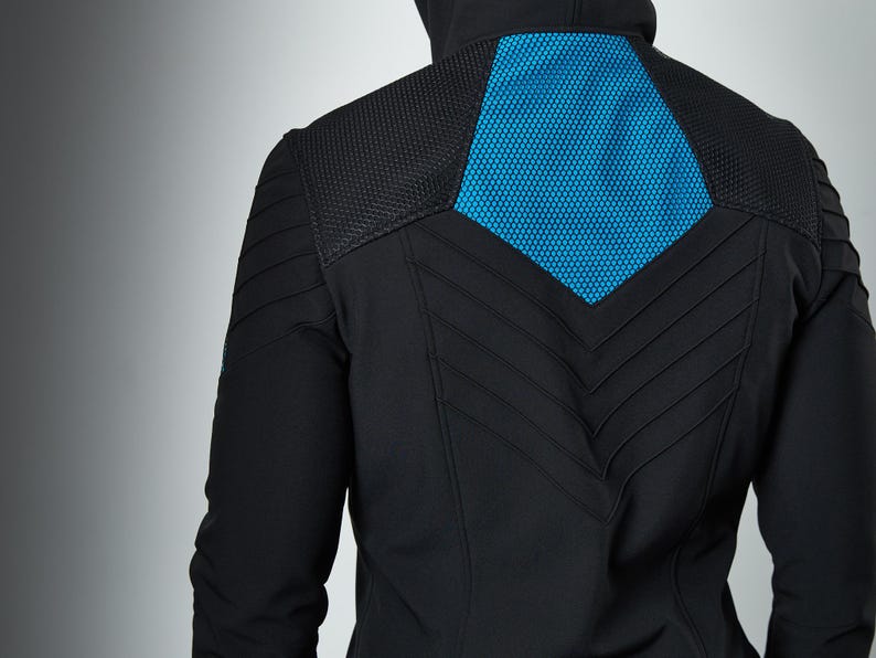 May include: A black hooded jacket featuring a vibrant blue hexagonal mesh panel on the upper back. The garment includes textured shoulder sections and a series of stitched chevron-style lines running down the center of the back panel.