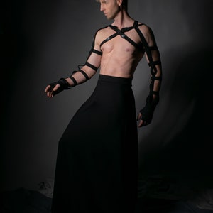 Man in black SK-L skirt and arm harness on dark background – performance outfit