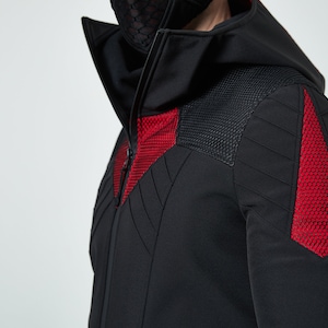 May include: A black hooded jacket featuring a high collar and a full-length front zipper. The garment includes textured red mesh panels on the chest and shoulders, complemented by black quilted stitching details across the upper sleeves and torso.