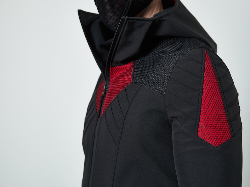 May include: A black hooded jacket featuring a high collar and a full-length front zipper. The garment includes textured red mesh panels on the chest and shoulders, complemented by black quilted stitching details across the upper sleeves and torso.