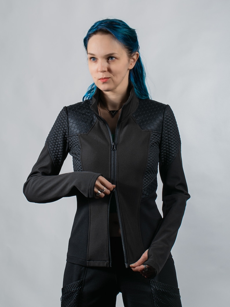 May include: A black zippered jacket with a textured design on the shoulders and sleeves. The jacket has a high collar and a slim fit.