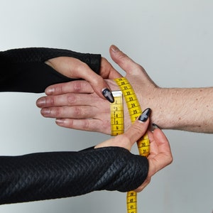 May include: A yellow measuring tape is being used to measure a person's wrist. The tape is wrapped around the wrist and the numbers on the tape are visible.